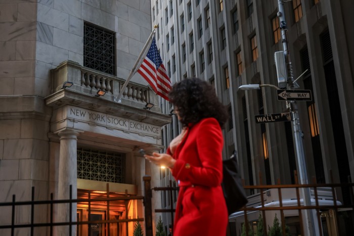 A woman in a red dress walks pas the front of the New York Stock Exchange entrance