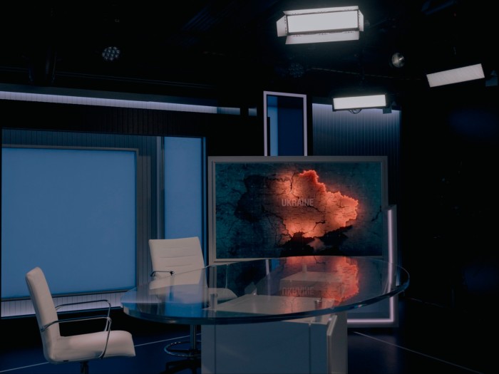 A studio with two chairs and a glass table as well as a screen featuring a map of Ukraine