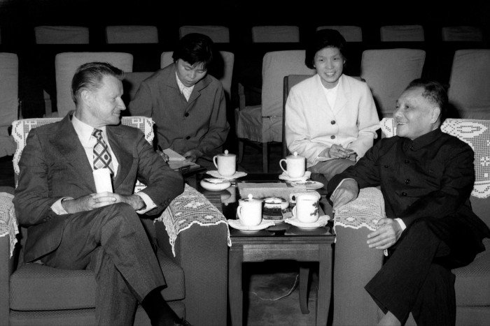 A black and white photoraph of four people sitting down drinking tea