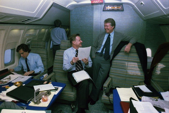 Four men in suits in the inside of a plane