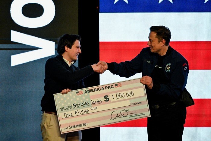 Elon Musk gives a check to an audience member during a rally in support of a conservative state Supreme Court candidate of an April 1 election in Green Bay, Wisconsin