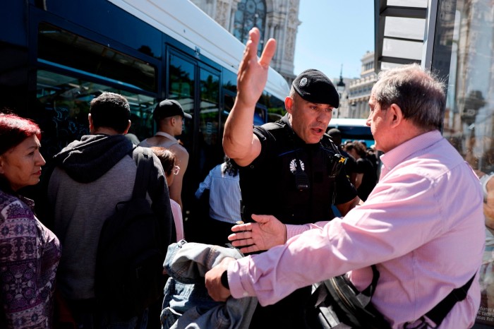 A Spanish policeman tries to keep people calm as they queue to catch a bus at the Plaza de Cibeles in Madrid
