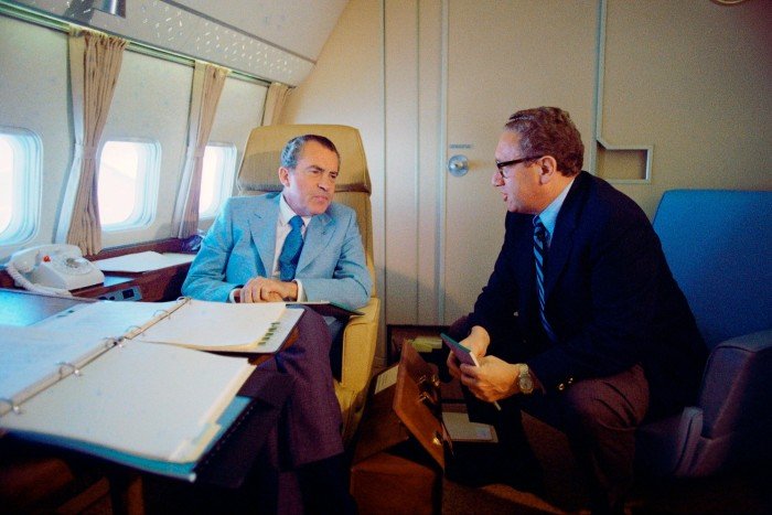 Two men in suits in a plane chatting