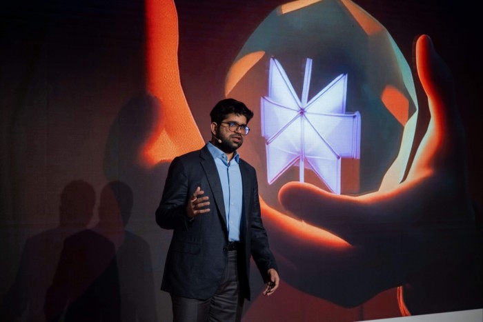 Aravind Srinivas stands on stage and speaks at an event