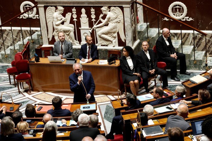 Francois Bayrou speaks at a podium during a debate in the French National Assembly, with officials seated behind him.