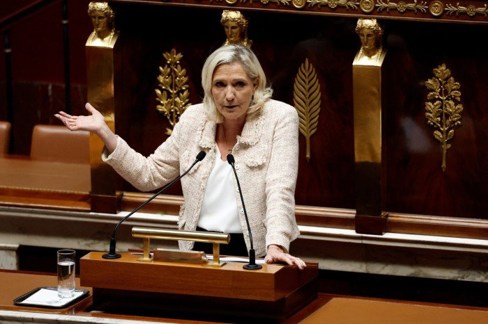 Marine Le Pen gestures while speaking at a podium during a debate in the French National Assembly.