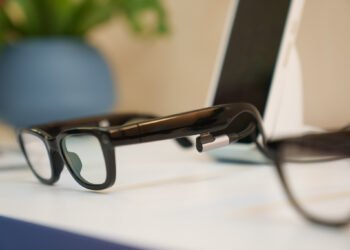 Close up of Google’s Prototype AI glasses from a side angle at Google I/O. In the background you can see a smartphone and vase with plants.