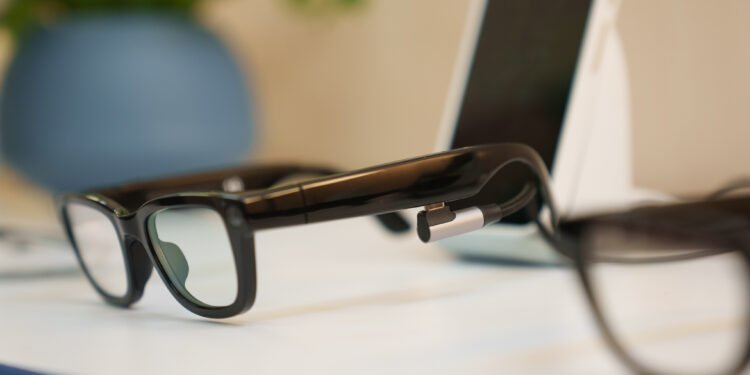 Close up of Google’s Prototype AI glasses from a side angle at Google I/O. In the background you can see a smartphone and vase with plants.
